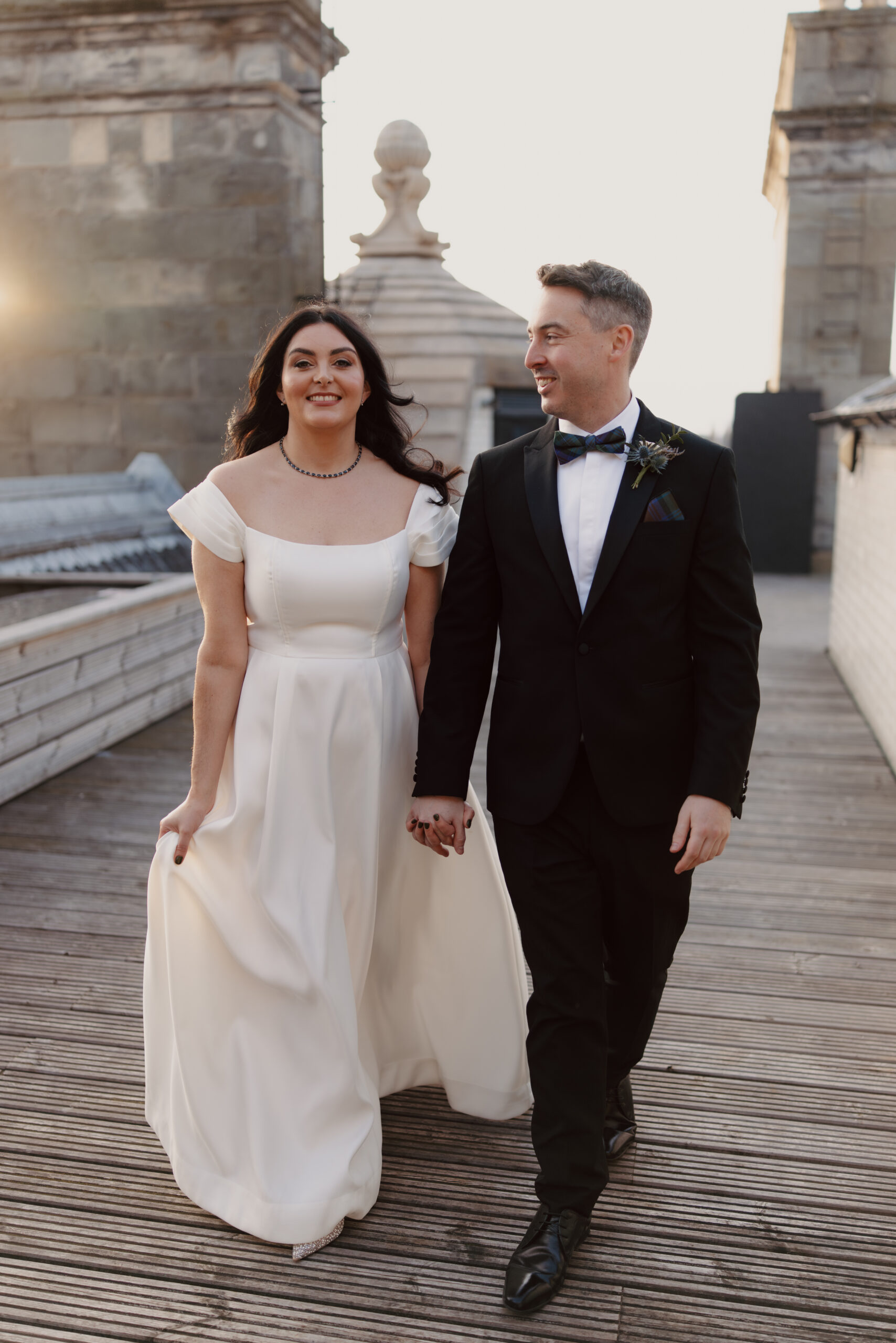 Bride and groom on rooftop at sunset walking hand in hand