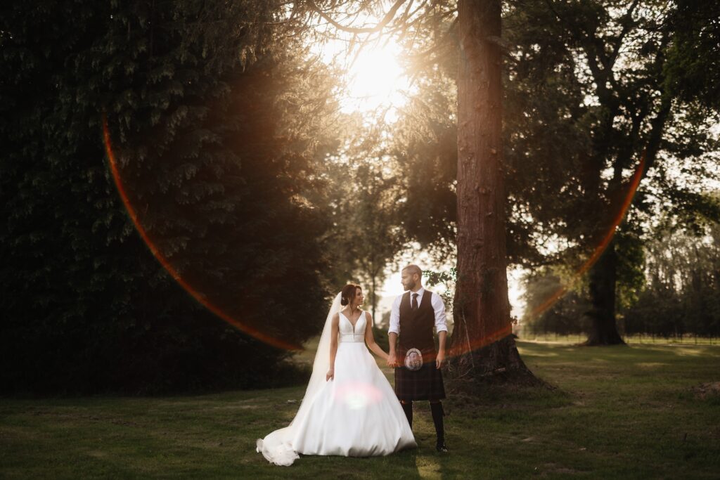 bride and groom in grounds of luxury estate at sunset the sun flares through the trees