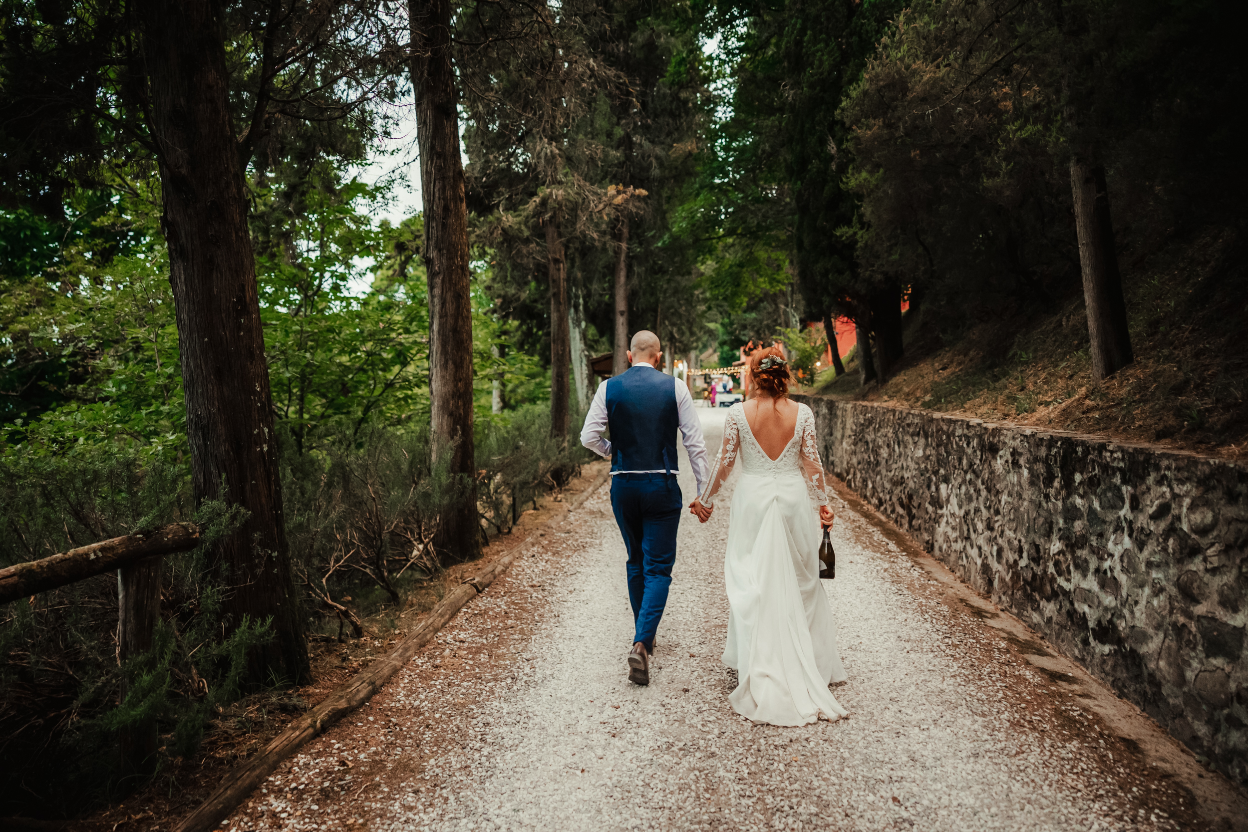 bride and groom walk along driveway lined by trees